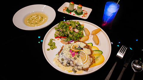 A plated main course, side salad and a blue cocktail on a dark table, from the Tapestree dining menu.
