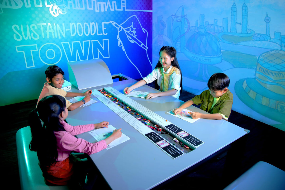 Four children colouring at the Sustain-Doodle Town drawing table at Petrosains.