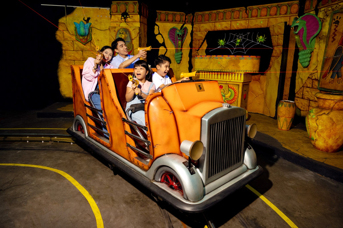 A family of four riding an orange LEGO car through an Egyptian-themed dark ride, with painted snakes and scarabs on the walls.