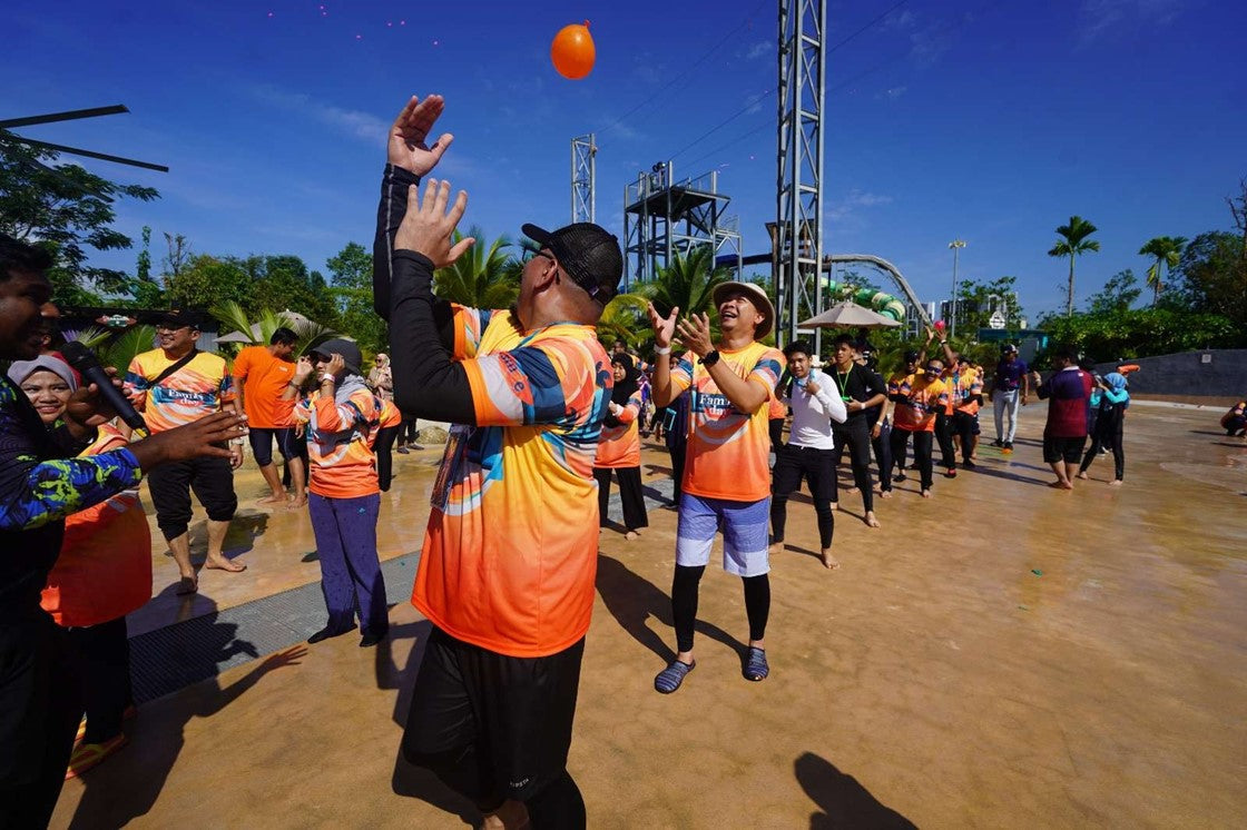 Visitors in orange and blue shirts playing a ball game on the poolside.