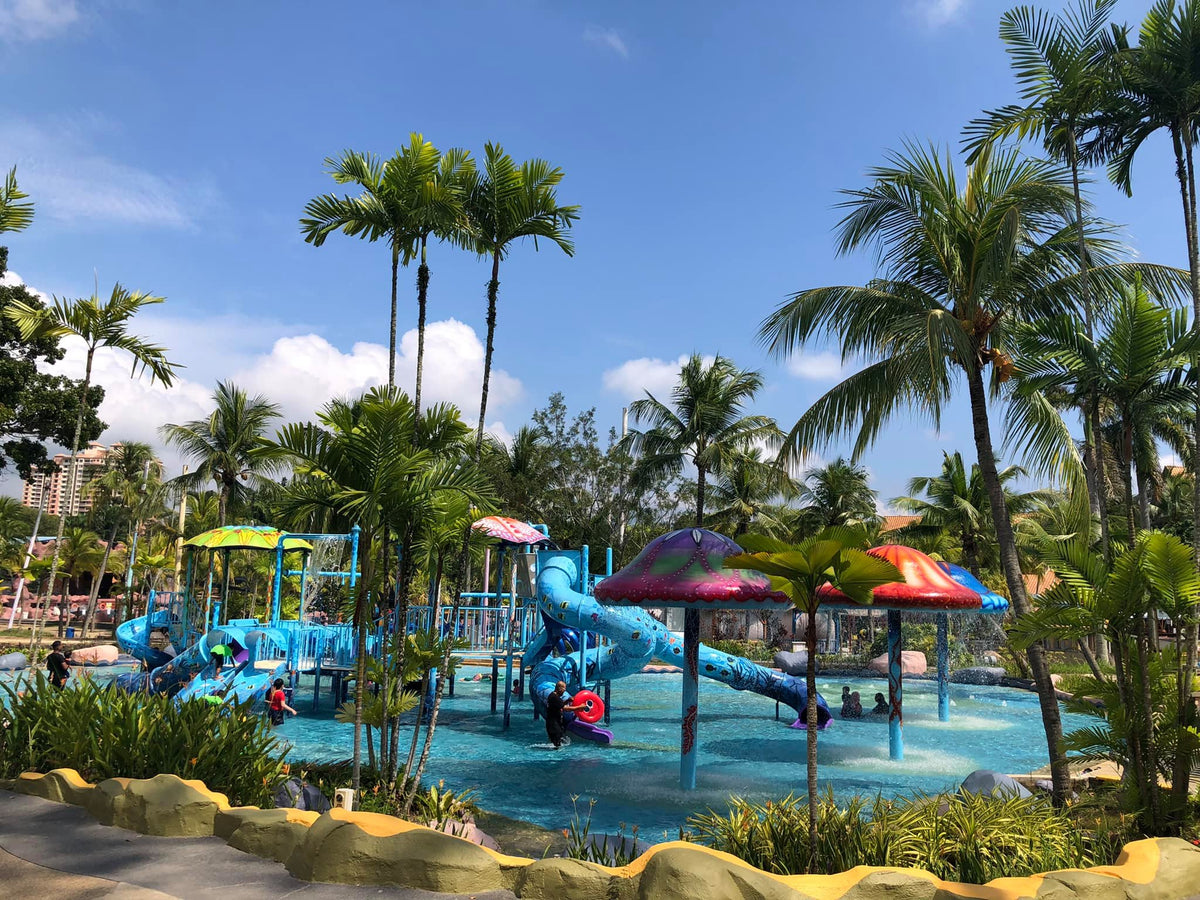 A children's water play area with coloured umbrellas and shallow pools, ringed by palms.