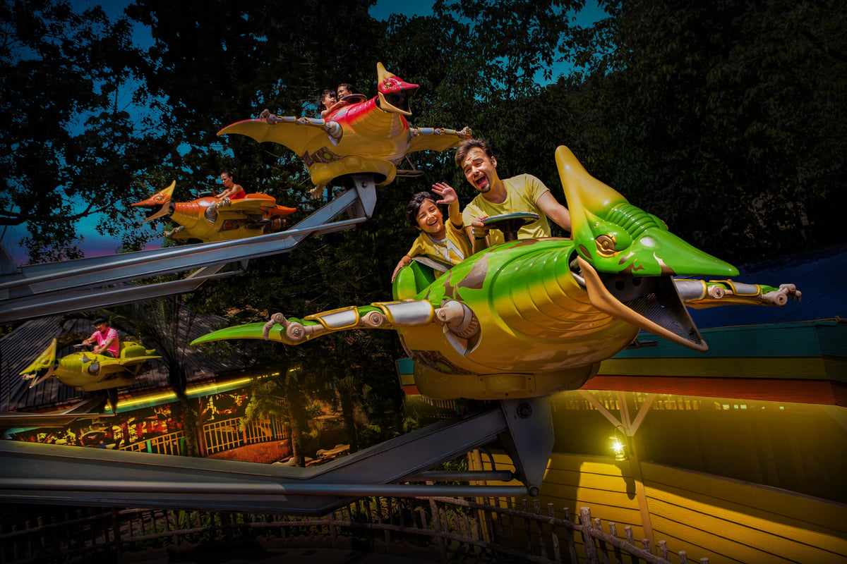 Riders on a flying-machine ride at night, seats banking over the lit track.