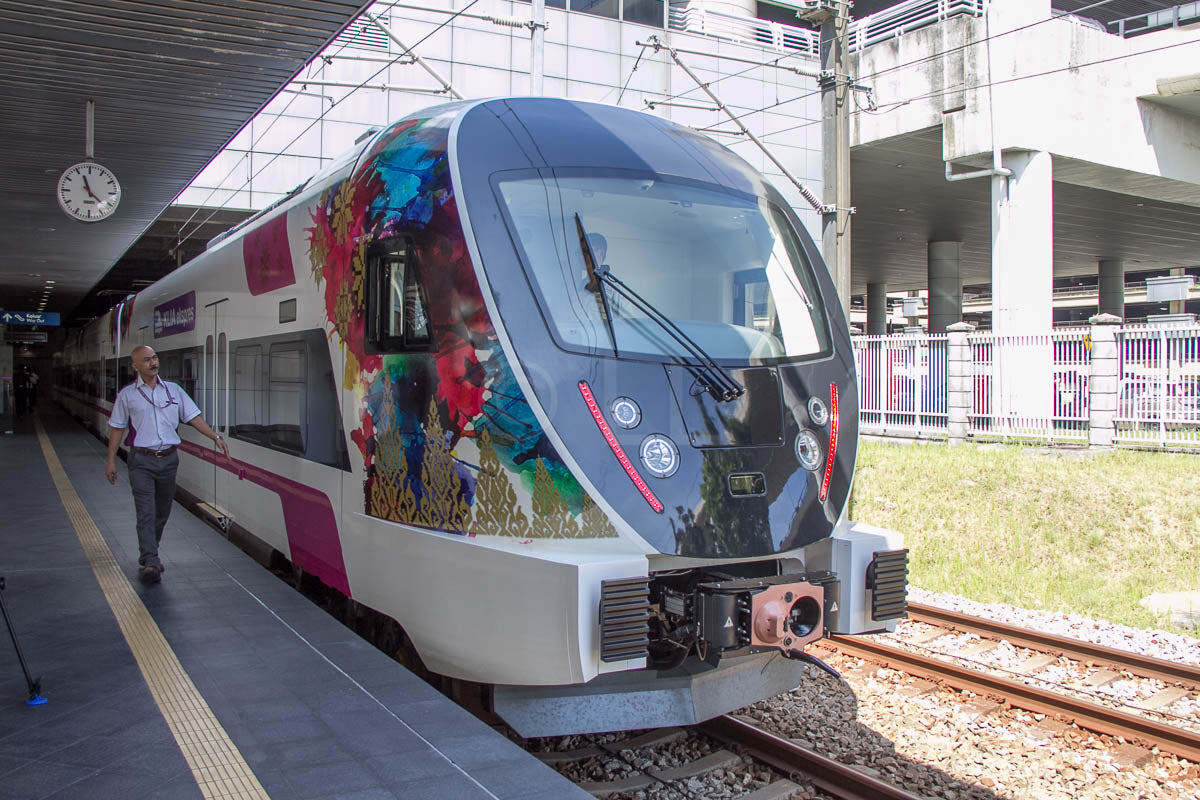 A KLIA Ekspres train with floral artwork at a platform, a member of staff walking past.