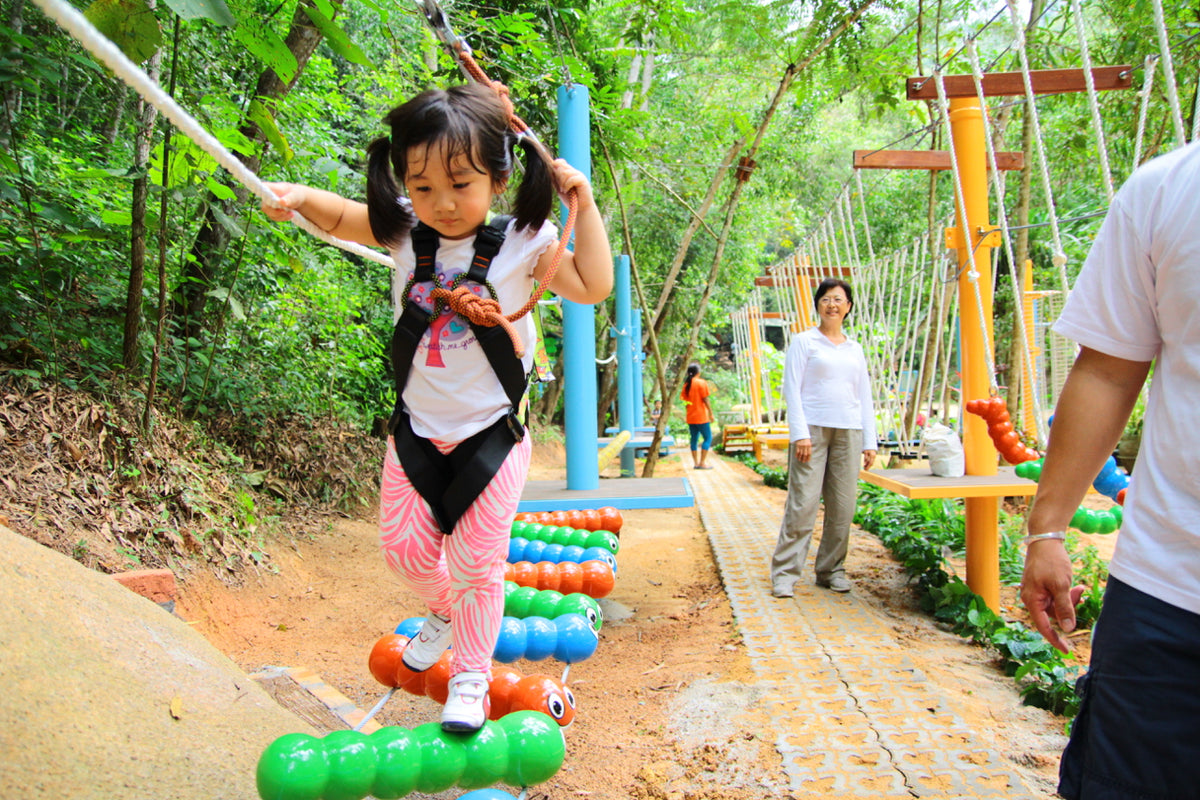 A girl in a safety harness stepping across a line of colourful caterpillar-shaped stepping barrels on a rope course.