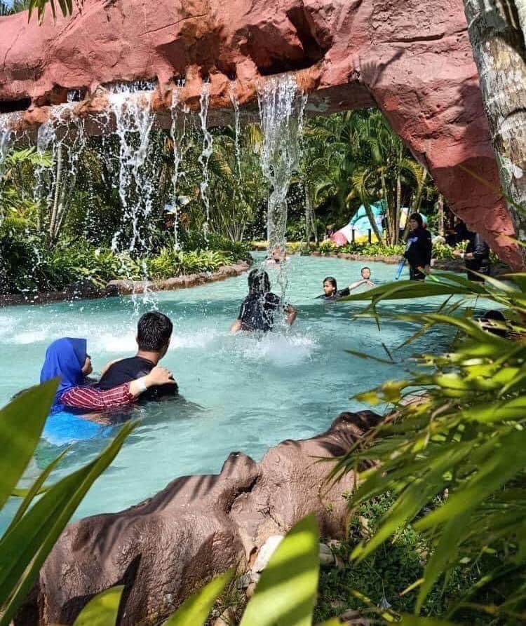 Swimmers under a rock waterfall in a turquoise pool fringed with palms.