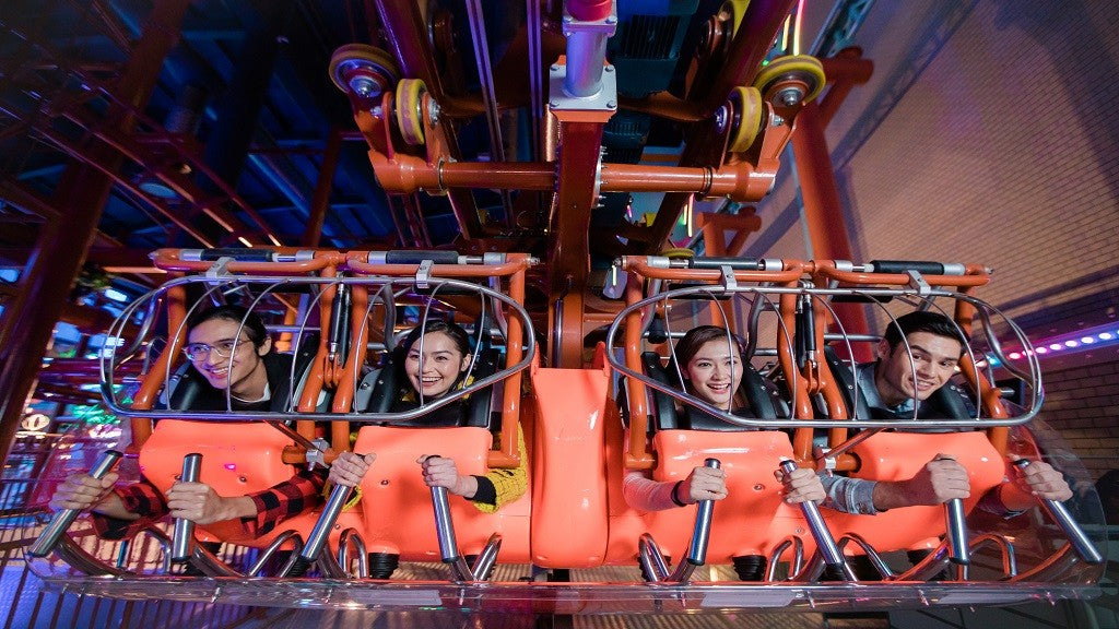 Riders strapped into a red indoor roller coaster car, mid-ride.