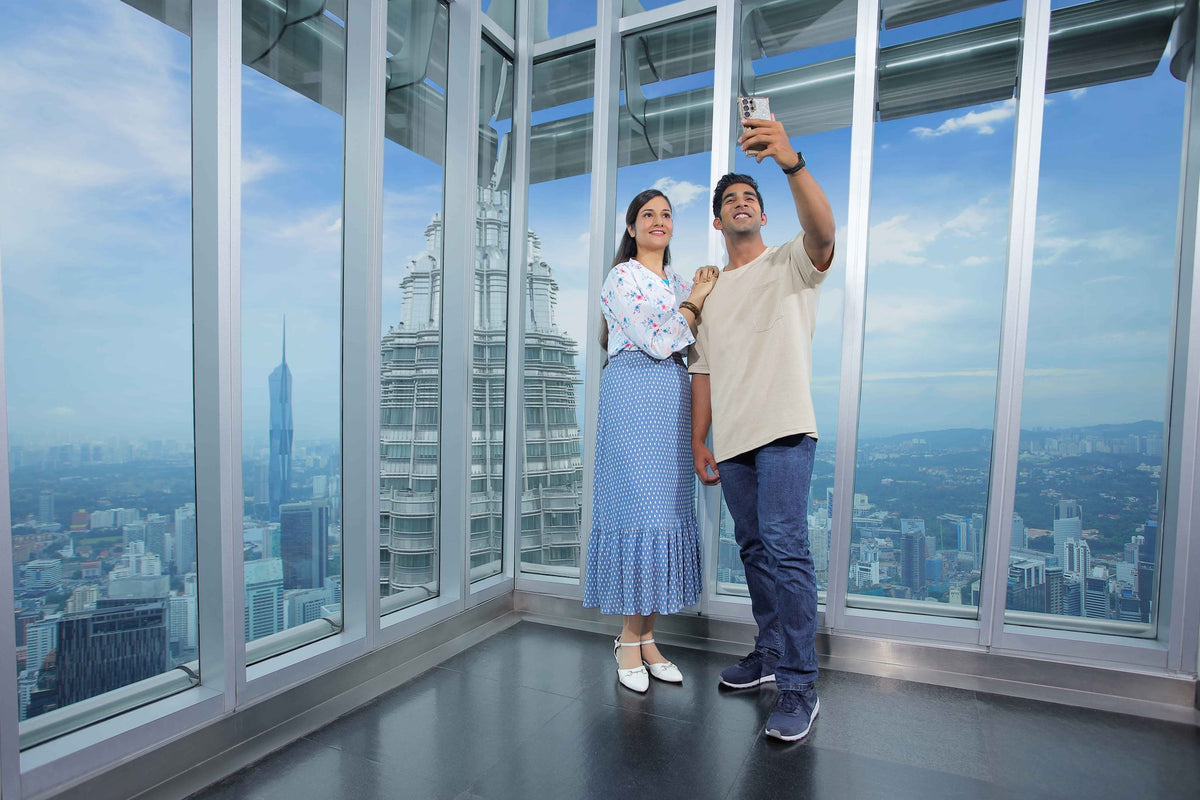 A couple photographing themselves in the corner window of the Observation Deck, looking out over Kuala Lumpur.