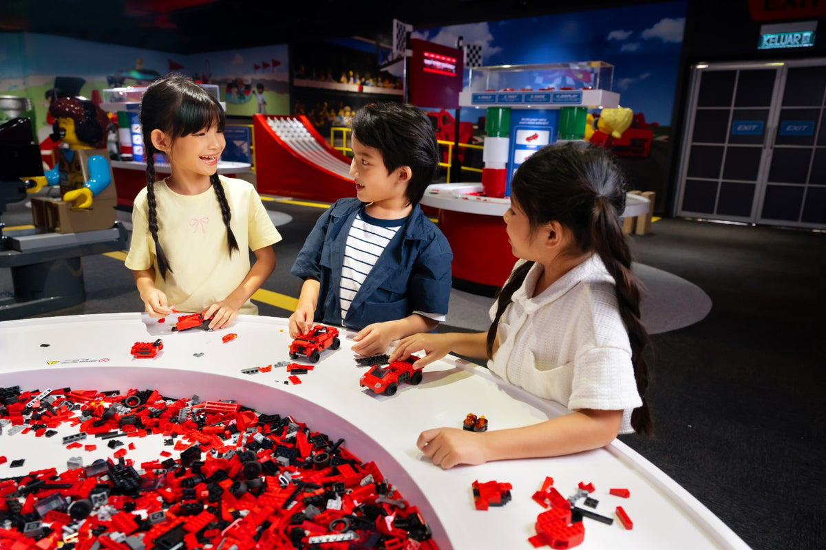 Three children building red LEGO race cars at a white curved table in the Ferrari Build and Race area.
