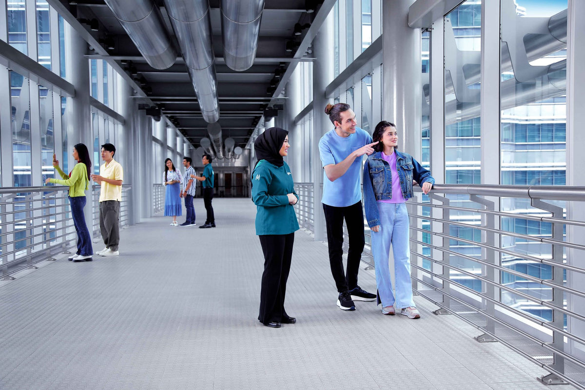 A guide on the Skybridge talking to a couple at the handrail while other visitors look out behind them.