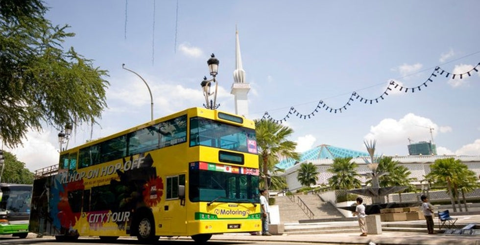 A yellow open-top bus at a stop with KL Tower rising behind it.