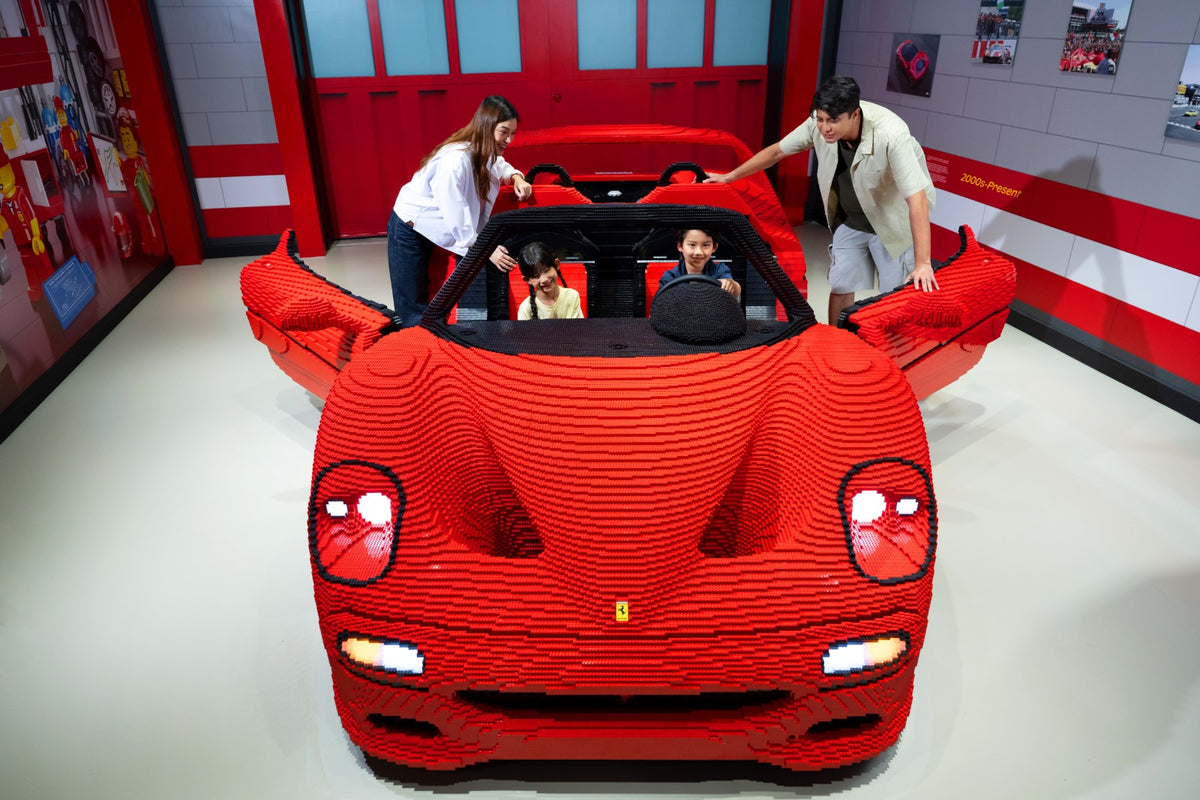 A life-size red LEGO Ferrari sports car with visitors around it in the Ferrari Build and Race gallery.