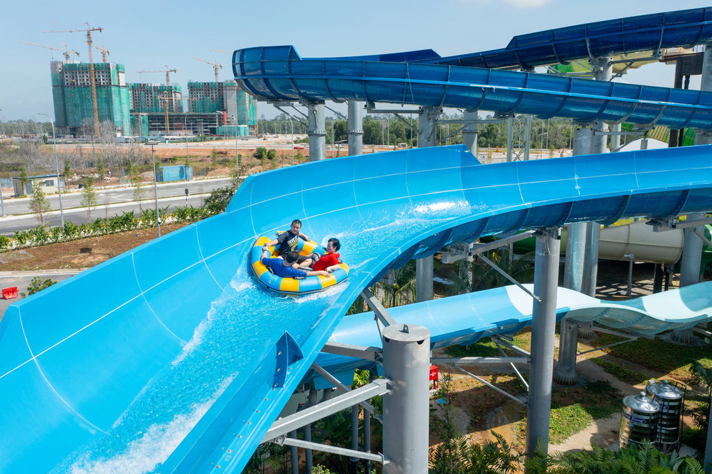 Four riders on a tube rounding a bend of a wide blue slide.
