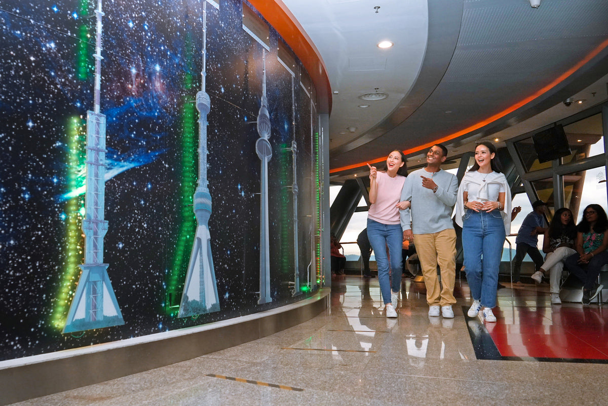 Visitors walking past an illuminated display of world towers inside the observation level.