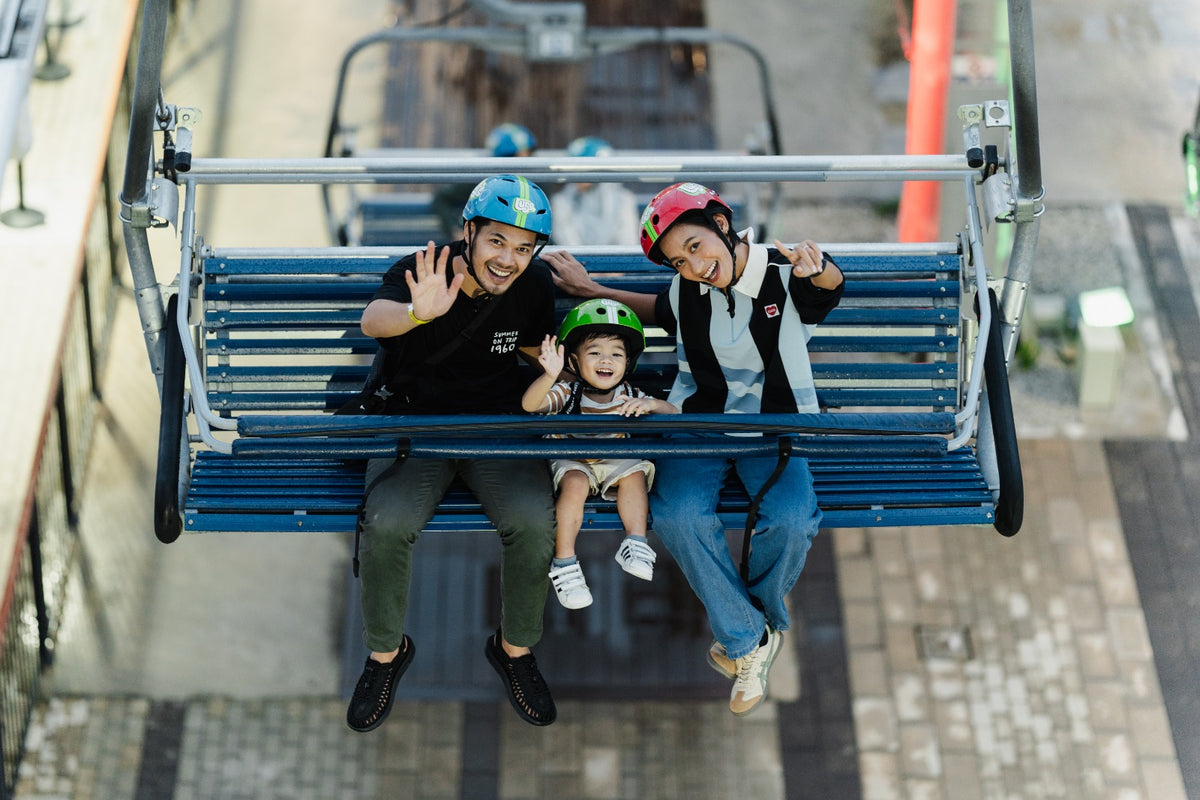 Overhead view of two adults and a small child waving from a Skyride chairlift.