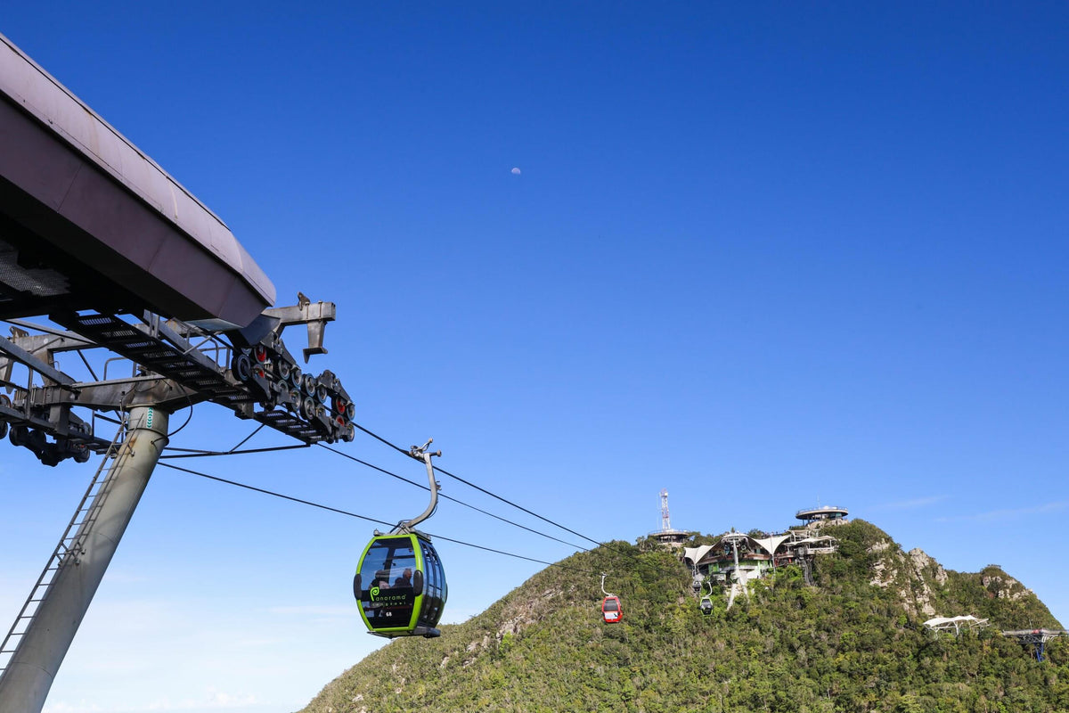 A green gondola leaving the station tower, the summit buildings on the ridge beyond.