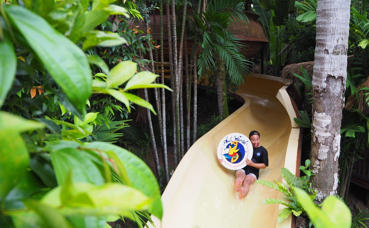 A member of staff at the mouth of a cream enclosed slide, holding a Wet World sign.
