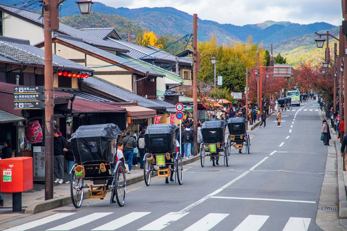 Rickshaws waiting on the main street at Arashiyama in Kyoto, with autumn hills rising behind the shopfronts.