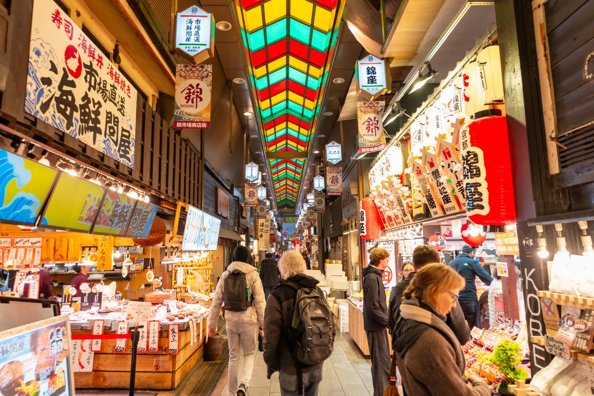 Shoppers in the covered arcade at Nishiki Market in Kyoto, beneath its stained-glass roof and hanging lanterns.