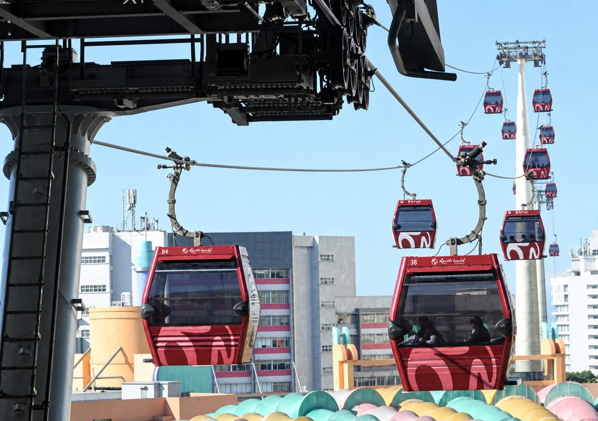 Resorts World Genting gondolas leaving the cable car station, passengers aboard, with the hilltop resort buildings and a support pylon behind.